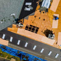 A roofer nailing shingles with air gun, replacing roof cover protection being applied, apartment development